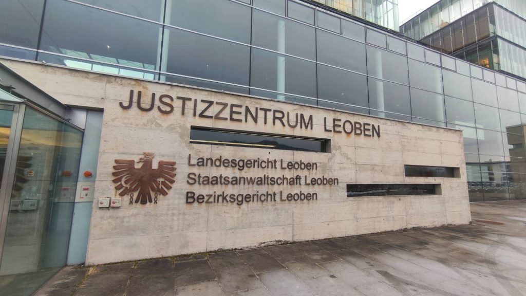 Foto vom Gericht in Leoben, zu sehen ist vor allem die Steinmauer am Einfang mit der Beschriftung: Justizzentrum Leoben, Landesgericht Leoben, Staatsanwaltschaft Leoben, Bezirksgericht Leoben und links dem Bundeswappen / Adler